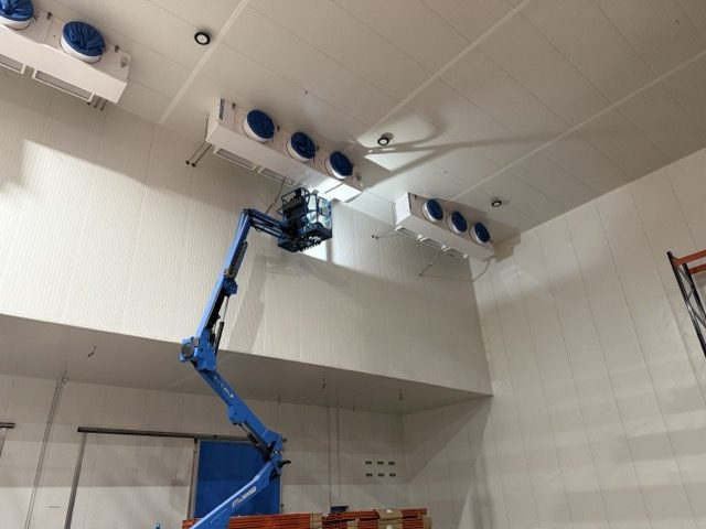 Évaporateurs installés en hauteur dans une chambre froide, nacelle élévatrice au premier plan