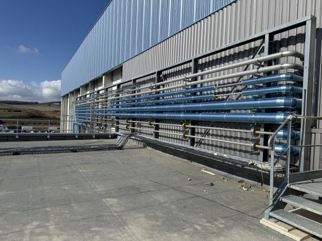 Réseaux de tuyauterie calorifugés le long de la façade d'un bâtiment frigorifique en chantier